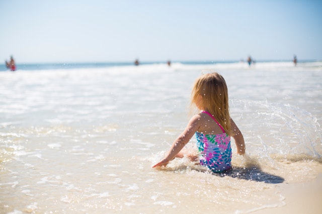 Dievčatko vo farebných plavkách sedí na pláži a hrá sa v mori.jpg