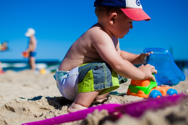Malý chlapček sa hrá s hračkami a formičkami v piesku na pieskovej pláži.jpg